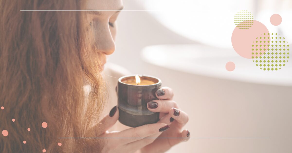 Woman holding and smelling a lit candle in a quiet, reflective setting.